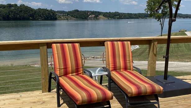 Eine Holzterrasse mit zwei gestreiften Liegestühlen, die auf einen See ausgerichtet sind.