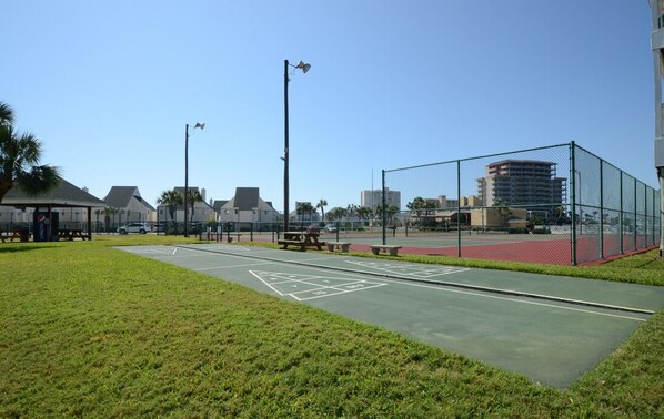 Una cancha de tenis con una red, rodeada por una valla, y una mesa de picnic cerca.