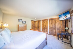 Ein Schlafzimmer mit einem großen Bett, einem Holzschrank, einem Schreibtisch mit Stuhl und einem an der Wand befestigten Fernseher.
