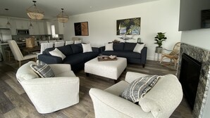 Un salon moderne avec un canapé d’angle, deux fauteuils, une table basse et une cheminée.
