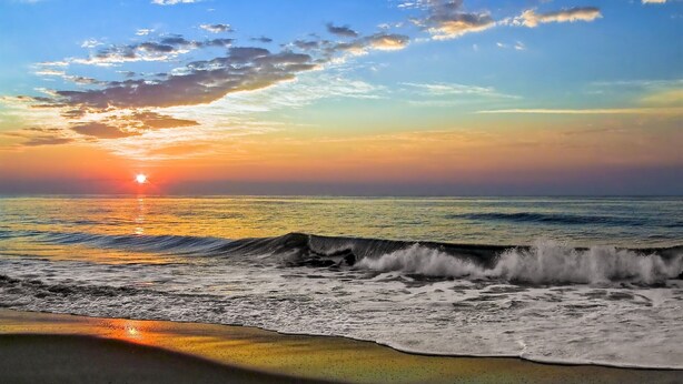 Une plage avec des vagues et un coucher de soleil.
