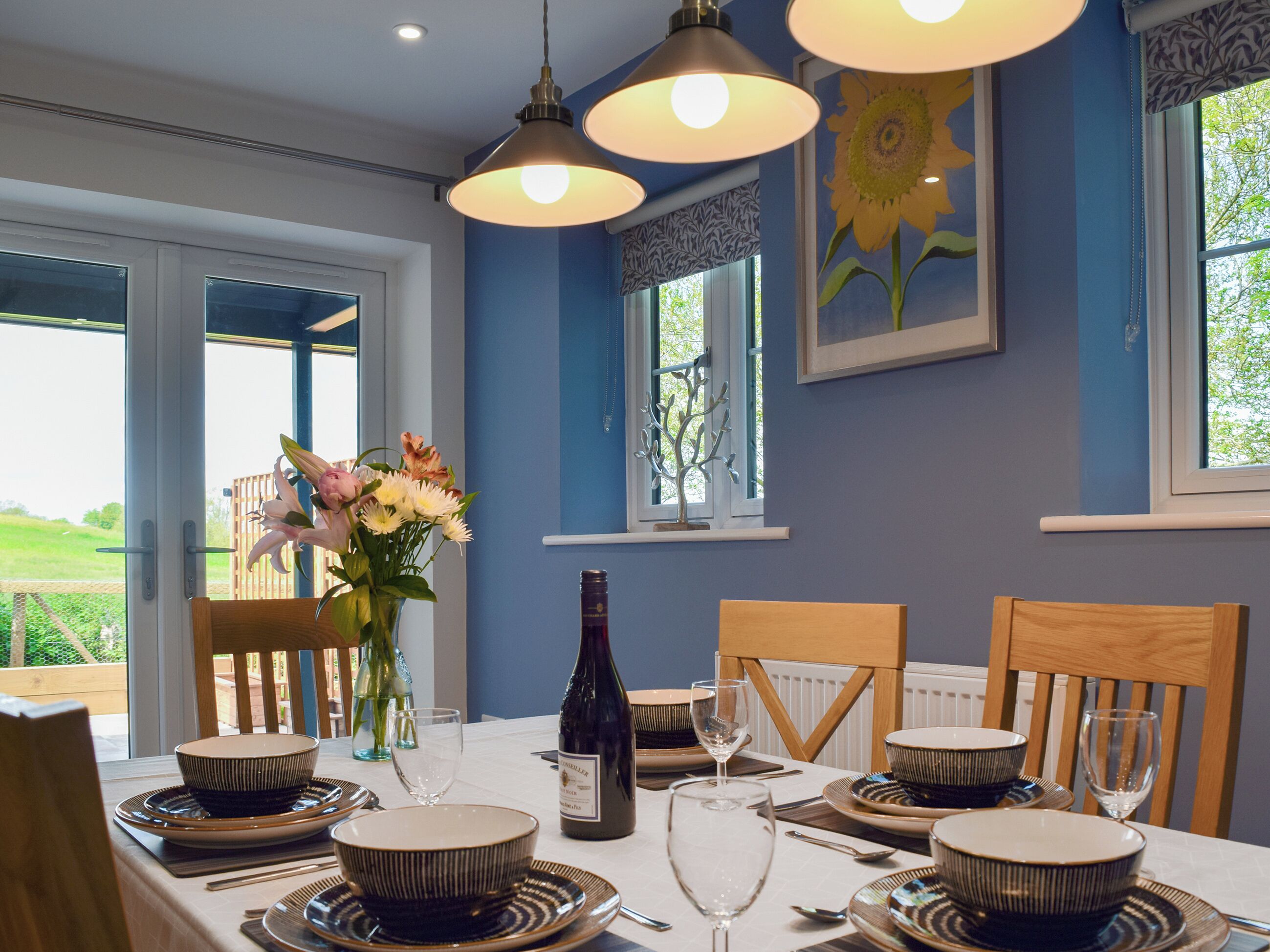 Un coin repas avec une table dressée pour six personnes, agrémenté de bols et d’assiettes à rayures, d’une bouteille de vin et d’un vase rempli de fleurs.