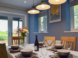 Un comedor con una mesa dispuesta para seis personas, con cuencos y platos a rayas, una botella de vino y un jarrón con flores.