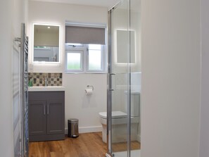 Un baño moderno con cabina de ducha de vidrio, inodoro y lavamanos con espejo.