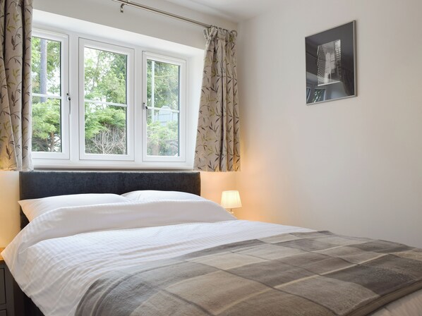 A bedroom with a bed, a window with curtains, a wall-mounted lamp, and a framed picture.