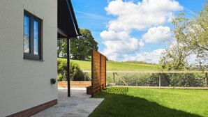 Et moderne hus med en overdækket terrasse, udsigt over landskabet og en klar himmel.