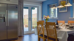 Et moderne køkken med et indbygget køleskab, et spiseområde med træstole og et bord dækket til to, samt en stor skydedør, der fører ud til en terrasse.