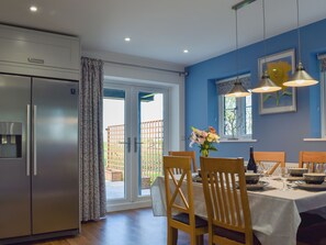 A modern kitchen with a built-in refrigerator, a dining area with wooden chairs and a table set for two, and a large sliding glass door leading to a patio. - 3 bedroom accommodation in Steventon, near Oxford (Steventon, near Oxford)