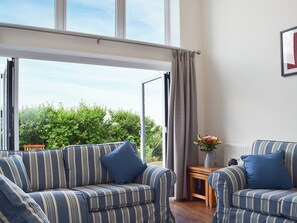 Una habitación con dos sofás a rayas, una pequeña mesa de madera con un florero y vistas a la vegetación a través de un ventanal grande.