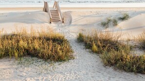 Une plage de sable avec un escalier en bois menant à un point plus élevé.