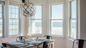 Un coin repas avec une table dressée pour quatre personnes, de grandes fenêtres offrant une vue sur la mer et un lustre sphérique unique.