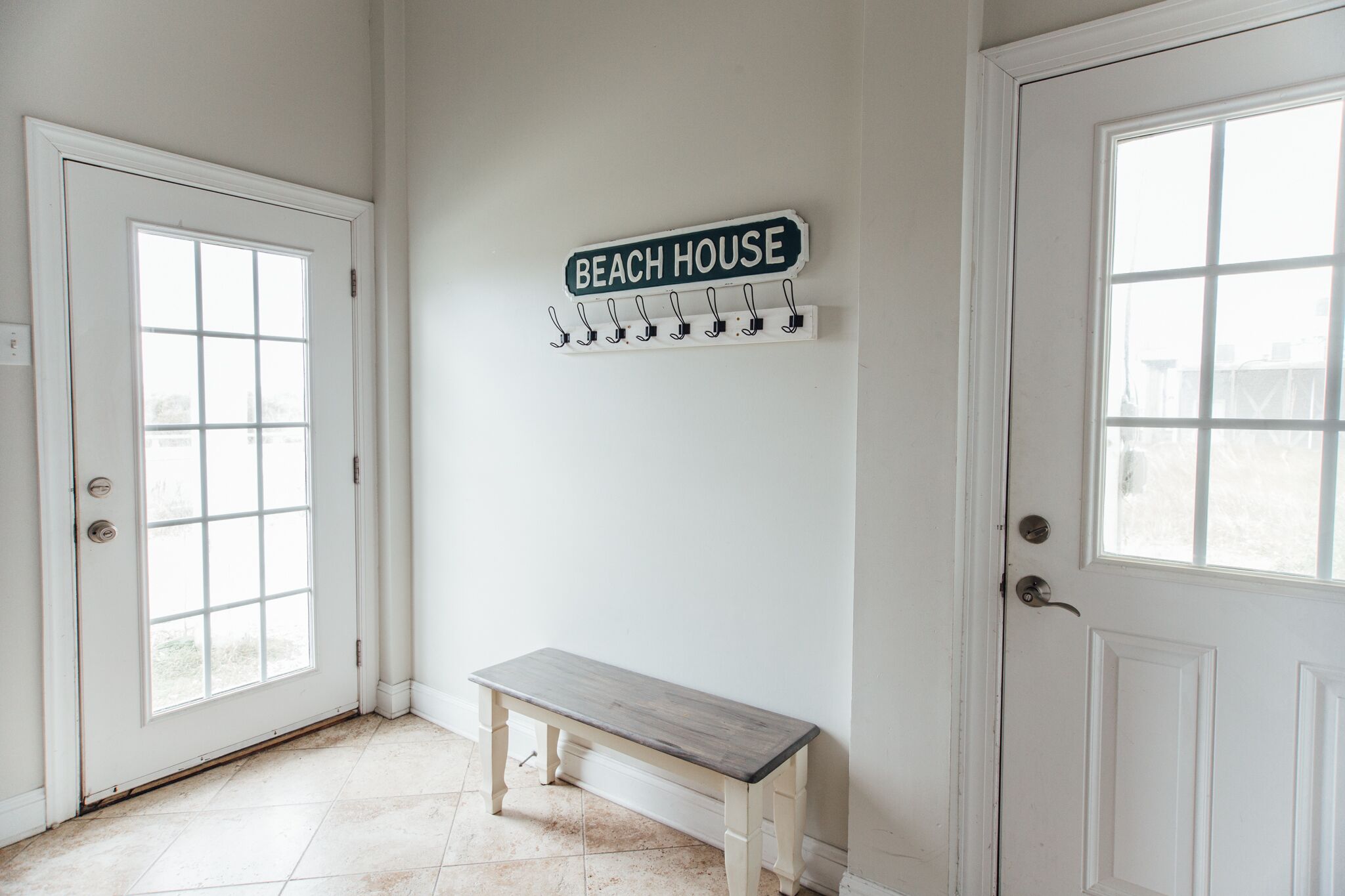Een witte ruimte met een bank, een deur waarop “BEACH HOUSE” staat en een kapstok met haken.