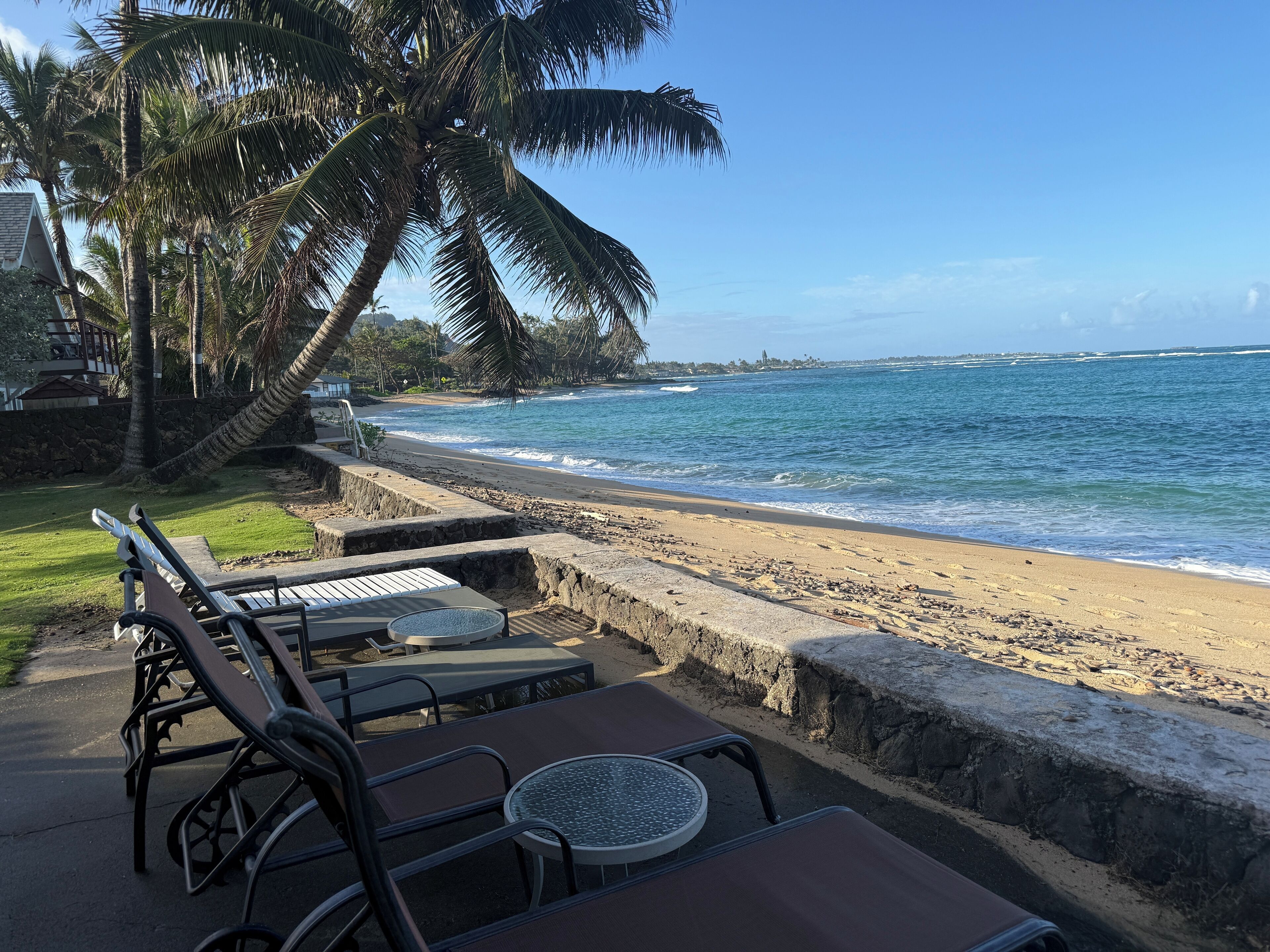 A beachside patio with lounge chairs and a table, overlooking the ocean.