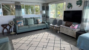 Un salon avec un canapé vert, deux fauteuils, un téléviseur et un ventilateur de plafond.