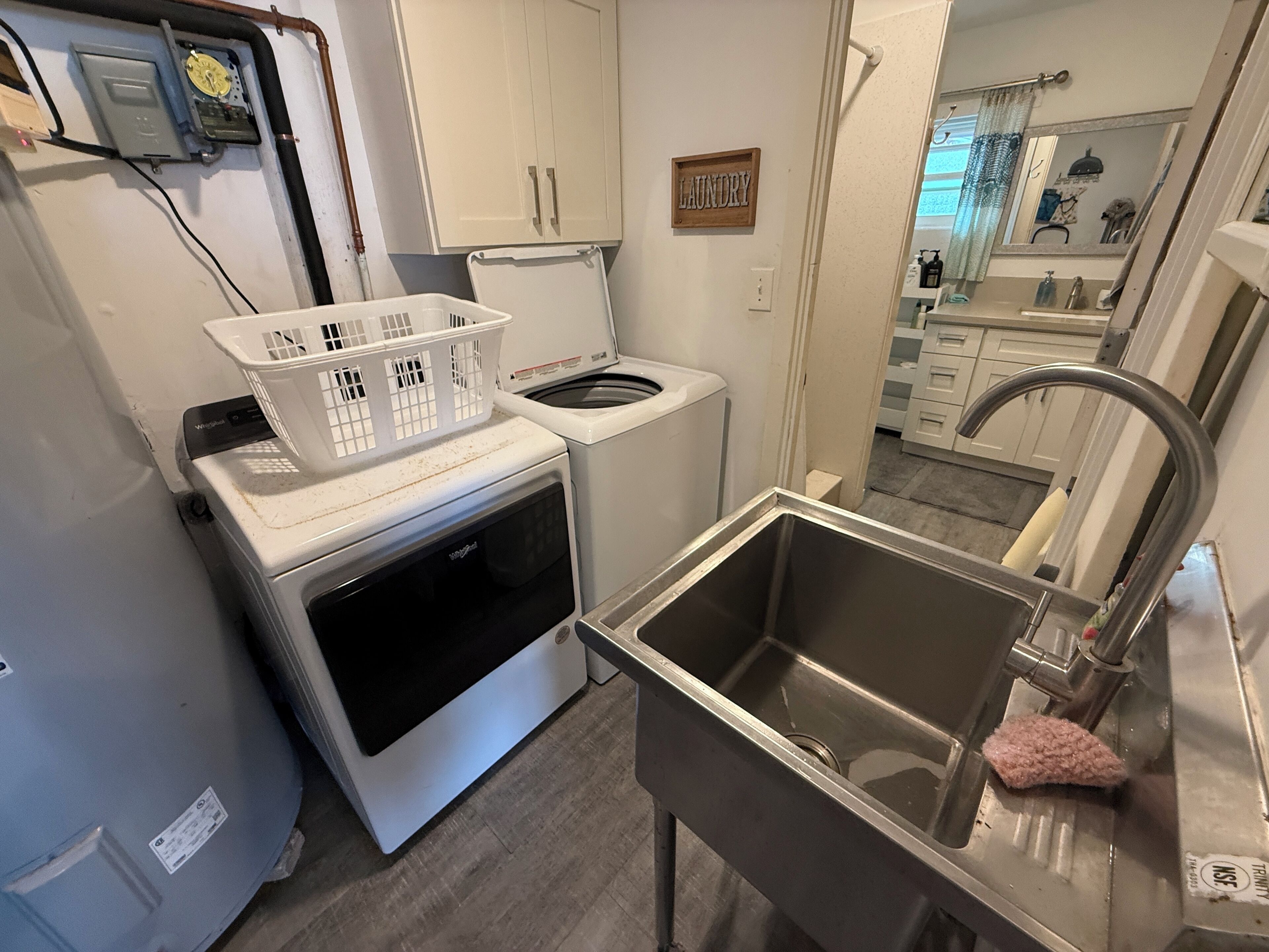 Una cocina compacta con lavadora y secadora integradas, un lavamanos de acero inoxidable y una cesta de ropa en la encimera.