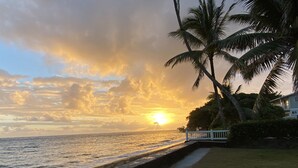 Un coucher de soleil sur l’océan, avec des palmiers et une clôture blanche le long de la plage.