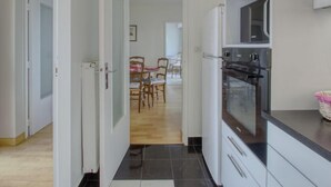 Ett modernt kök med inbyggd ugn och mikrovågsugn, en matplats med bord och stolar samt en hall som leder till ett annat rum.