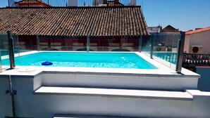 Una piscina al terrat amb aigua transparent de color blau, envoltada d'una estructura de vidre, i un teulat emblat al fons.