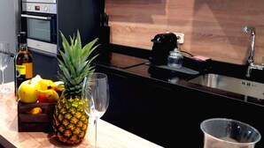 Una cuina amb un taulell, una ampolla de vi Solos, una pinya i un bol de fruita.