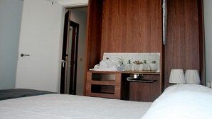 Habitació d'hotel amb un llit, un taulell de fusta amb mirall i una petita zona d'estar amb una banca.