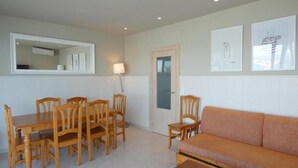 A dining area with a wooden table and chairs, a sofa, and a door with a mirror above it. - Rentalmar Family Acantilados (Salou)