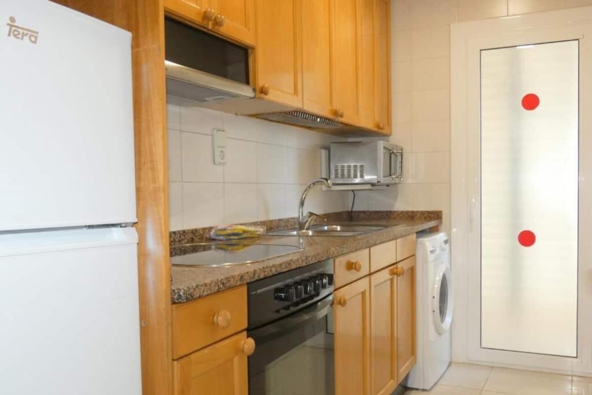 A kitchen with wooden cabinets, a built-in microwave, a sink, and a washing machine.
