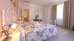 Un dormitorio con colcha estampada, una lámpara de noche y vista a un baño por una puerta abierta.