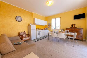 Un espace de vie compact comprenant un canapé, une table à manger, des chaises, un coin cuisine et un téléviseur à écran plat fixé au mur.