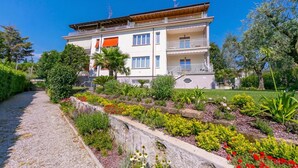 Un edificio de varios pisos con balcones, rodeado por un jardín ajardinado con diversas plantas y flores.