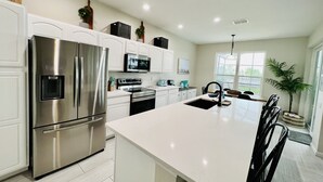 Een moderne keuken met roestvrijstalen apparatuur, witte keukenkastjes en een groot eiland met zitplaatsen.