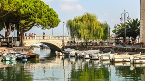 Un canal con barcos amarrados, un puente de piedra y árboles.