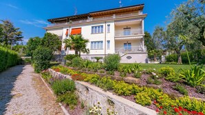 Un edificio de varios pisos con balcones, rodeado de un jardín ajardinado con diversas plantas y flores.