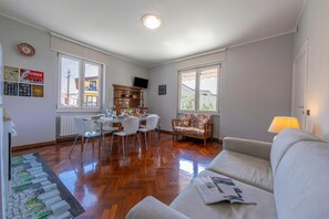 Un salon comprenant un canapé, une table à manger avec des chaises, un meuble en bois et un téléviseur fixé au mur.