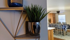 A small potted plant on a metal shelf in a room with a dining area in the background.