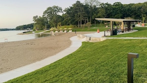 A beach with a grassy area, a walking path, and a covered seating area.