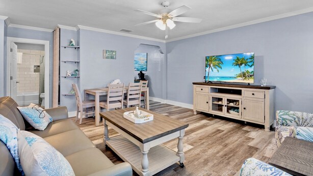 A living room with a wooden dining table, a sofa, a TV, and a ceiling fan. - Family Friendly Home, 4 mins to Beach! - Starfish Cove, B (Holmes Beach)
