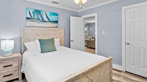 A bedroom with a wooden headboard, a bed with white bedding, a nightstand with a lamp, and a ceiling fan. - Family Friendly Home, 4 mins to Beach! - Starfish Cove, B (Holmes Beach)