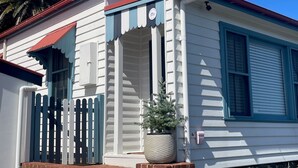 Uma casa branca com telhado vermelho, varanda azul e base de tijolos.