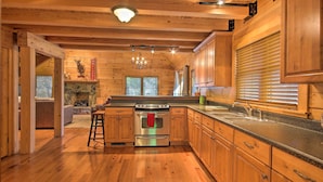 A wooden cabin-style kitchen with a central island, wooden cabinets, and a stone fireplace. - Peaceful Tignall Cabin on Strom Thurmond Lake! (Tignall)