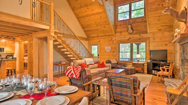 A spacious log cabin interior with a dining area, a living room with a fireplace, and a staircase leading to an upper level. - Peaceful Tignall Cabin on Strom Thurmond Lake! (Tignall)