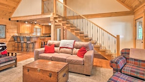 A spacious living area with a wooden staircase, a sofa with red cushions, and a plaid-patterned chair. - Peaceful Tignall Cabin on Strom Thurmond Lake! (Tignall)