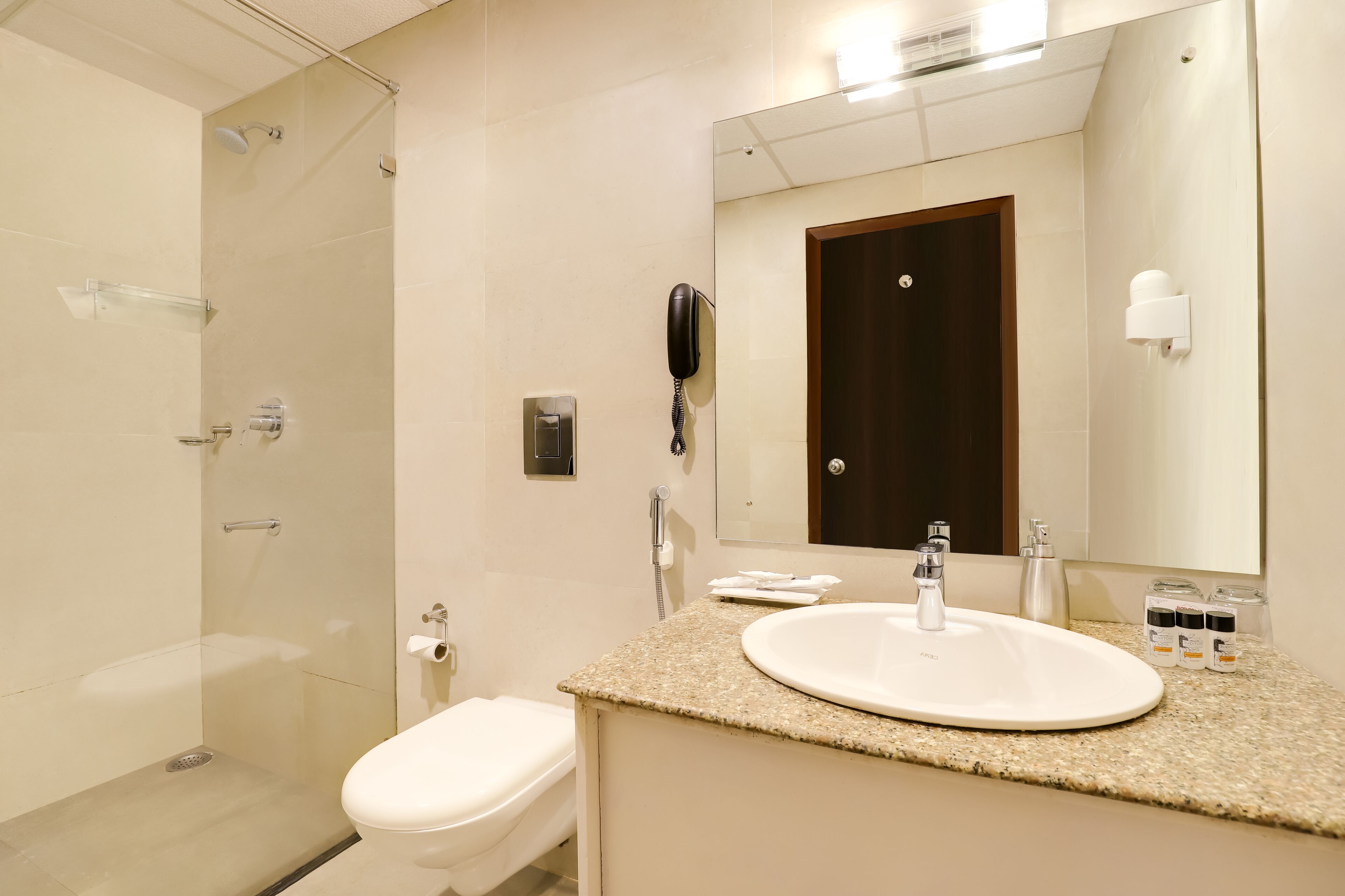 Une salle de bain moderne avec une douche à parois de verre, des toilettes blanches, un comptoir en granit, un lavabo, un miroir et un téléphone.