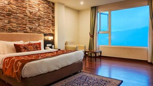 A hotel room with a large bed, a stone wall, a view of the sea, and a small table with a chair. - The Fern Denzong Hotel & Spa Gangtok (Gangtok)