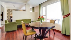 A modern living room with a round wooden table, green sofas, and a stone accent wall. - The Fern Denzong Hotel & Spa Gangtok (Gangtok)