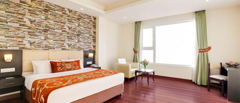 A hotel room with a stone wall, a large bed, a desk, and a chair.