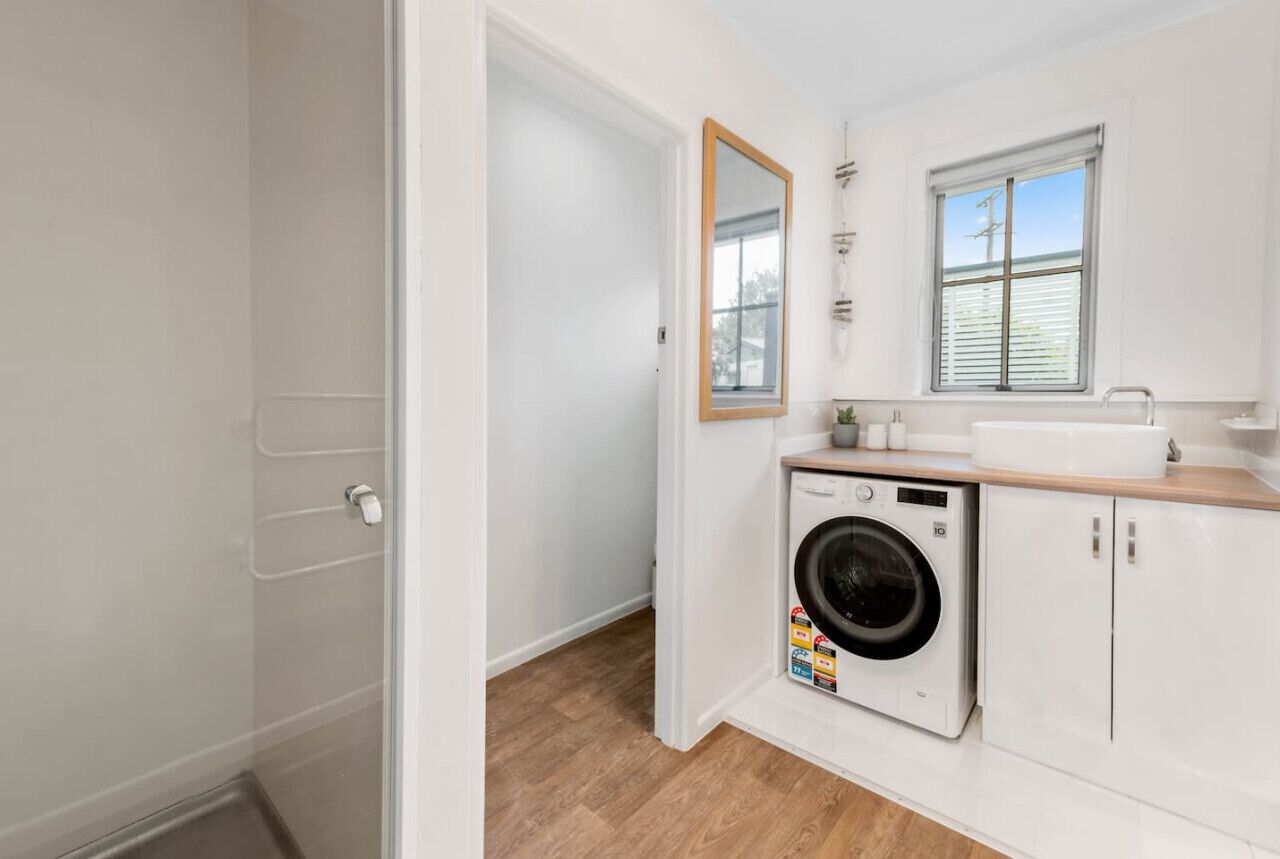 A compact laundry room with a washing machine, a sink, and a mirror.