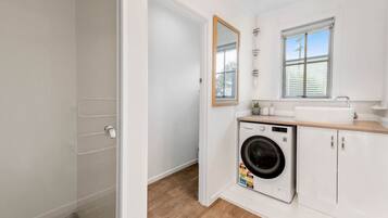 A compact laundry room with a washing machine, a sink, and a mirror.