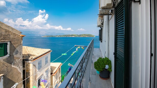 A balcony with a view of the sea, a potted plant, and a building with a tiled roof. - City walls sea view (Corfu)