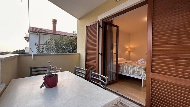 A balcony with a table and chairs, a potted plant, and a sliding door leading to a bedroom with a bed and a nightstand. - Apartment 823/1920 (Istria - Novigrad), 150m from the beach (Novigrad)