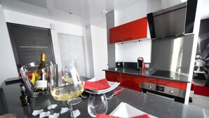 Una cocina moderna con armarios rojos, electrodomésticos de acero inoxidable y un comedor con copas de vino y una botella.